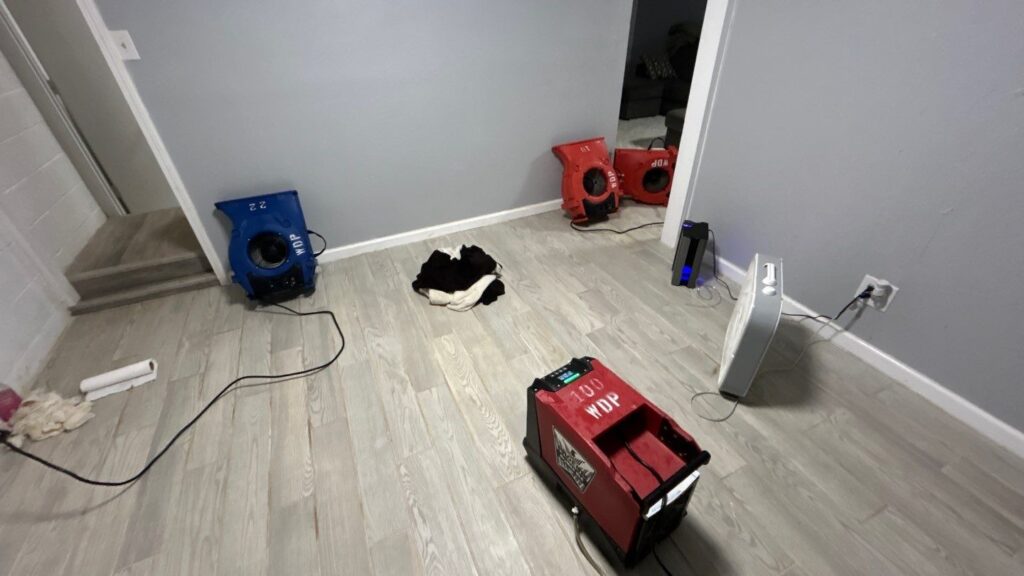 Professional water damage restoration equipment, including air movers and dehumidifiers, set up in a home to dry out floors and walls after water damage.