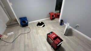 Professional water damage restoration equipment, including air movers and dehumidifiers, set up in a home to dry out floors and walls after water damage.