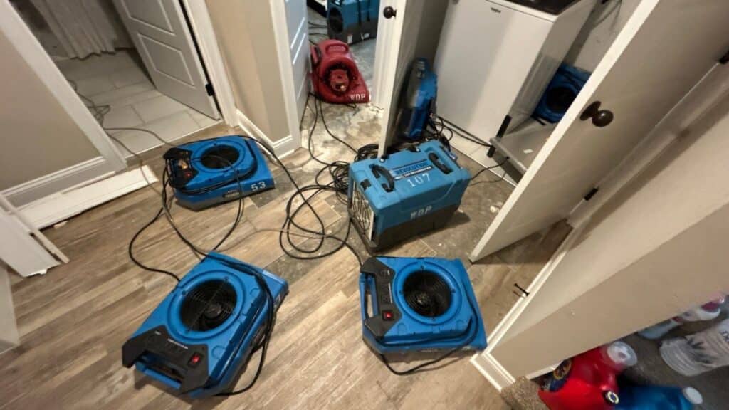 Water damage restoration in progress with industrial air movers and dehumidifiers drying a flooded home. Professional equipment is set up to remove excess moisture and prevent mold growth
