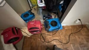 Multiple air movers and drying equipment set up in a residential closet area during water damage restoration to dry hardwood and carpet flooring.
