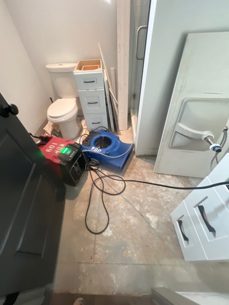 Water damage drying equipment in a bathroom, with an air mover and dehumidifier set up to dry wet tile flooring around the shower and vanity area.