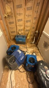 Wall water damage drying equipment set up near exposed insulation and plumbing